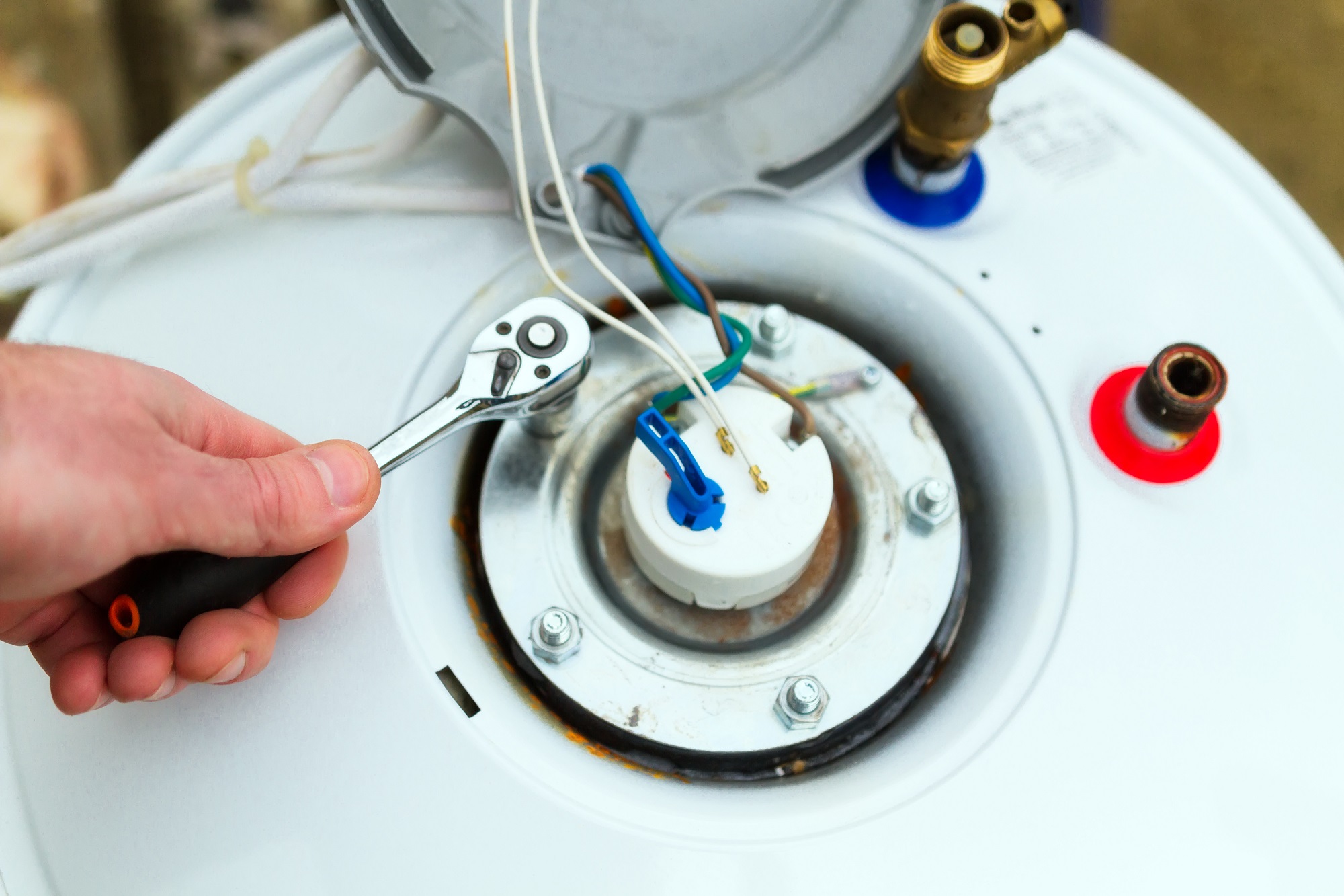 Technician performing tankless water heater service beside a Scarborough - ME utility wall with testing tools